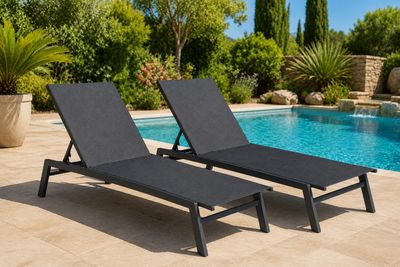 deux chaises longues noires au bord d'une piscine, avec des arbres en arrière-plan