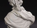 a white statue of a man sitting next to a vase