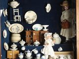 une vitrine contenant une poupée et remplie de porcelaine