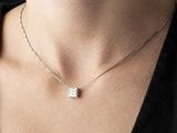 a woman wearing a silver necklace with a square pendant on it