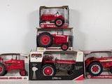 four red toy tractors in boxes on a white surface