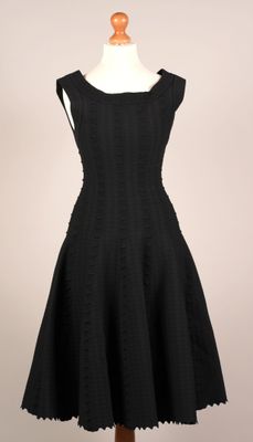 une robe noire posée sur un pied de mannequin, avec un mannequin blanc en arrière-plan
