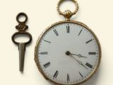 une montre de poche en or et une clé posées sur une surface blanche