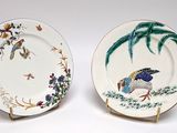 two plates with birds painted on them sitting on a table