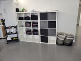 a room with a bookcase, shelves, and two bins on the floor