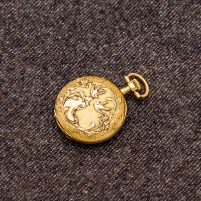 une image représentant une montre de poche en or posée sur un tissu marron