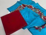 une écharpe bleue et un livre rouge posés sur une table blanche