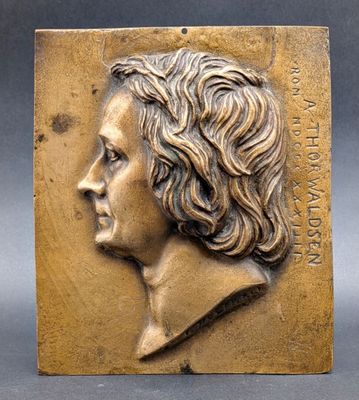 a bronze plaque of a woman ' s head with wavy hair