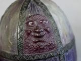 quelqu'un tient un vase violet sur lequel est dessiné un visage