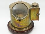 une théière ancienne en laiton reposant sur un socle en bois, sur fond blanc