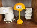 une lampe jaune posée sur une étagère à côté d'un seau