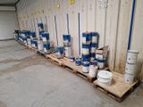 de nombreux seaux de peinture posés sur des palettes dans un entrepôt