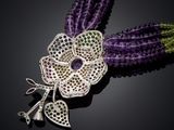 a close up of a purple flower broochle with green and purple beads