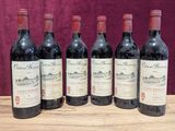 six bottles of red wine are lined up on a wooden table