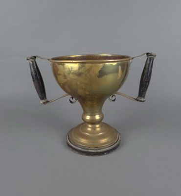 une coupe ancienne en laiton à deux anses, posée sur un socle