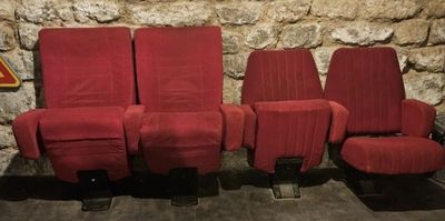 trois chaises rouges alignées les unes à côté des autres devant un mur de pierre