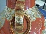 a large orange vase with a gold handle on a table