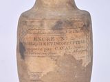 un vieux vase portant une inscription, posé sur une surface blanche
