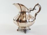 an image of a silver pitcher on a stand on a white surface