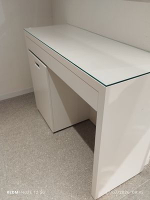 a white desk with a glass top in the corner of a room