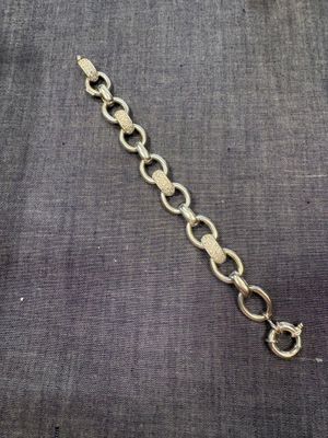 un gros plan d'un bracelet à maillons dorés posé sur un tissu gris