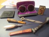 une table sur laquelle se trouvent divers objets, notamment un couteau, des lunettes de soleil et un étui