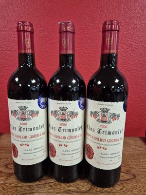 trois bouteilles de vin posées sur une table en bois, près d'un mur rouge