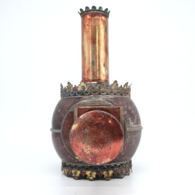 un vase rouge surmonté d'un couvercle doré, posé sur une surface blanche