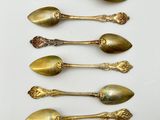 six antique spoons are lined up in a row on a white surface