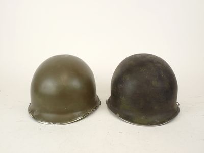 pair of wwii german steel helmets on a white background