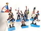 seven figurines of soldiers with flags on display on a white surface