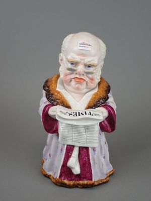 une vieille figurine représentant un homme tenant un journal dans ses mains