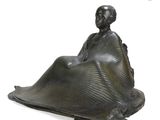 statue of a woman sitting on a blanket on a white surface