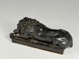 a bronze statue of a sleeping lion on a wooden base