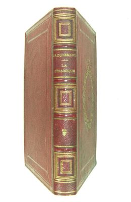 un vieux livre rouge avec des bordures dorées posé sur une surface blanche