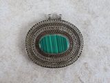 a close up of a silver and green broochle on a white surface