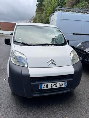 une petite camionnette blanche garée sur un parking à côté d'une voiture noire
