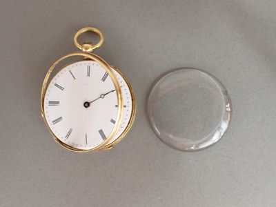 une montre de poche en or et un verre transparent posés sur la table
