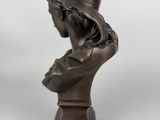 a bronze bust of a woman with a hat on her head
