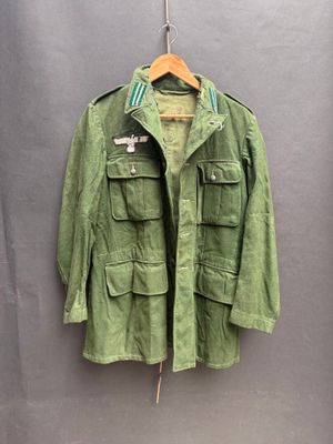 an army green jacket hanging on a hanger on a wall