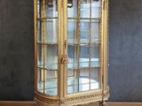 une vitrine ancienne dorée avec des portes vitrées, posée sur un parquet