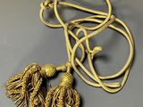 a close up of a gold necklace with two tassels on it