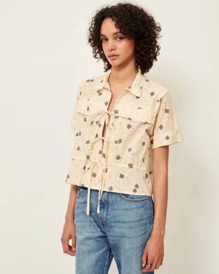 an image of a woman standing in front of a white wall wearing a shirt and jeans