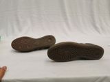 someone is holding a pair of brown shoes on a white surface