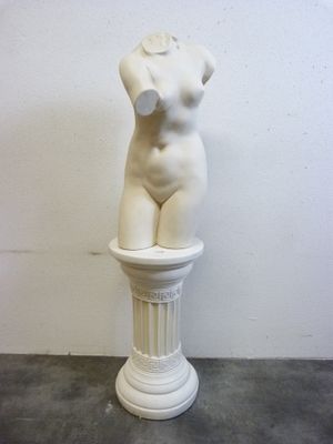 sculpture représentant un torse féminin posée sur un socle devant un mur blanc