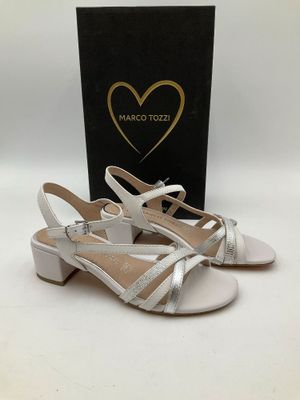 une paire de sandales blanches à lanières argentées et une boîte noire
