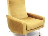 beige upholstered chair with metal legs and arm rests against a white wall