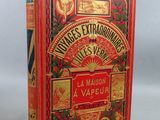 un livre rouge avec des lettres dorées posé sur une surface blanche