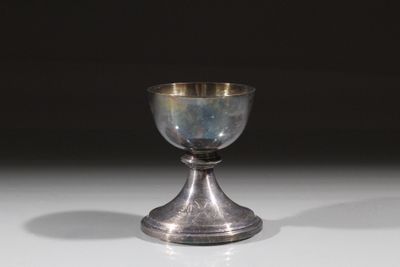 un gobelet en argent posé sur une table, sur fond noir
