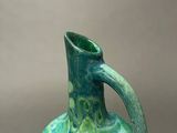 a green vase with leaves on it sitting on a table